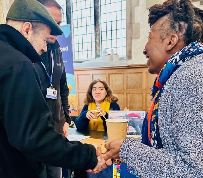 two carers shaking hands at an information day with stall holders